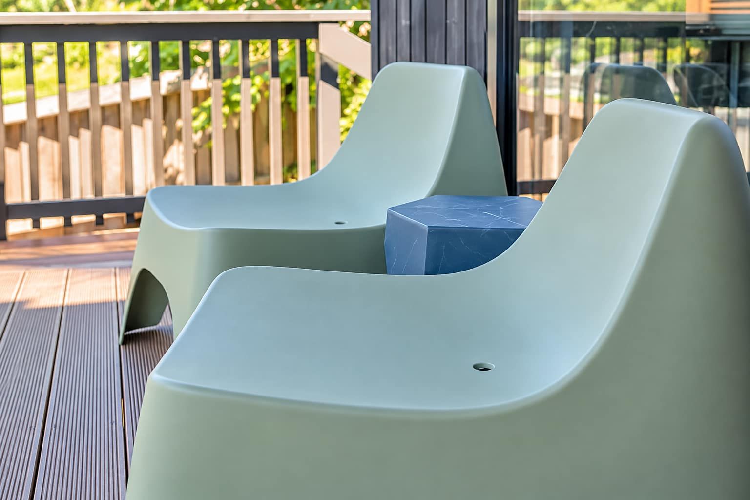 Two modern lounge chairs on a wooden deck with a view of a wooden fence and greenery.