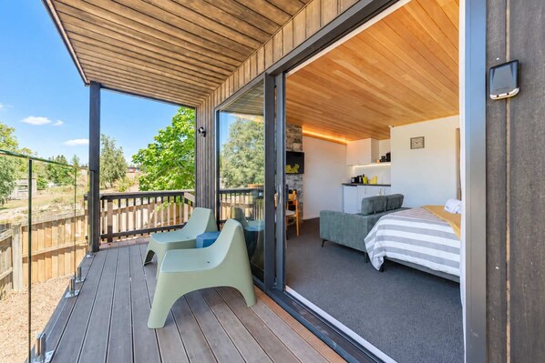 A modern room with a bed, a small kitchenette, and a balcony with two chairs.