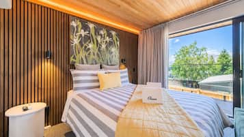 A modern hotel room with a large bed, a bedside table, a view of the outdoors, and a wooden ceiling.