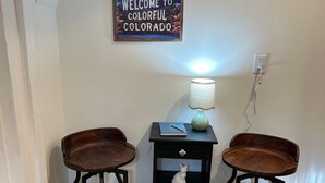Ein Zimmer mit zwei Holzsesseln, einem kleinen schwarzen Tisch mit einer Lampe, einem Schild mit der Aufschrift 'Welcome to Colorful Colorado' und einem Streifen Teppichboden.