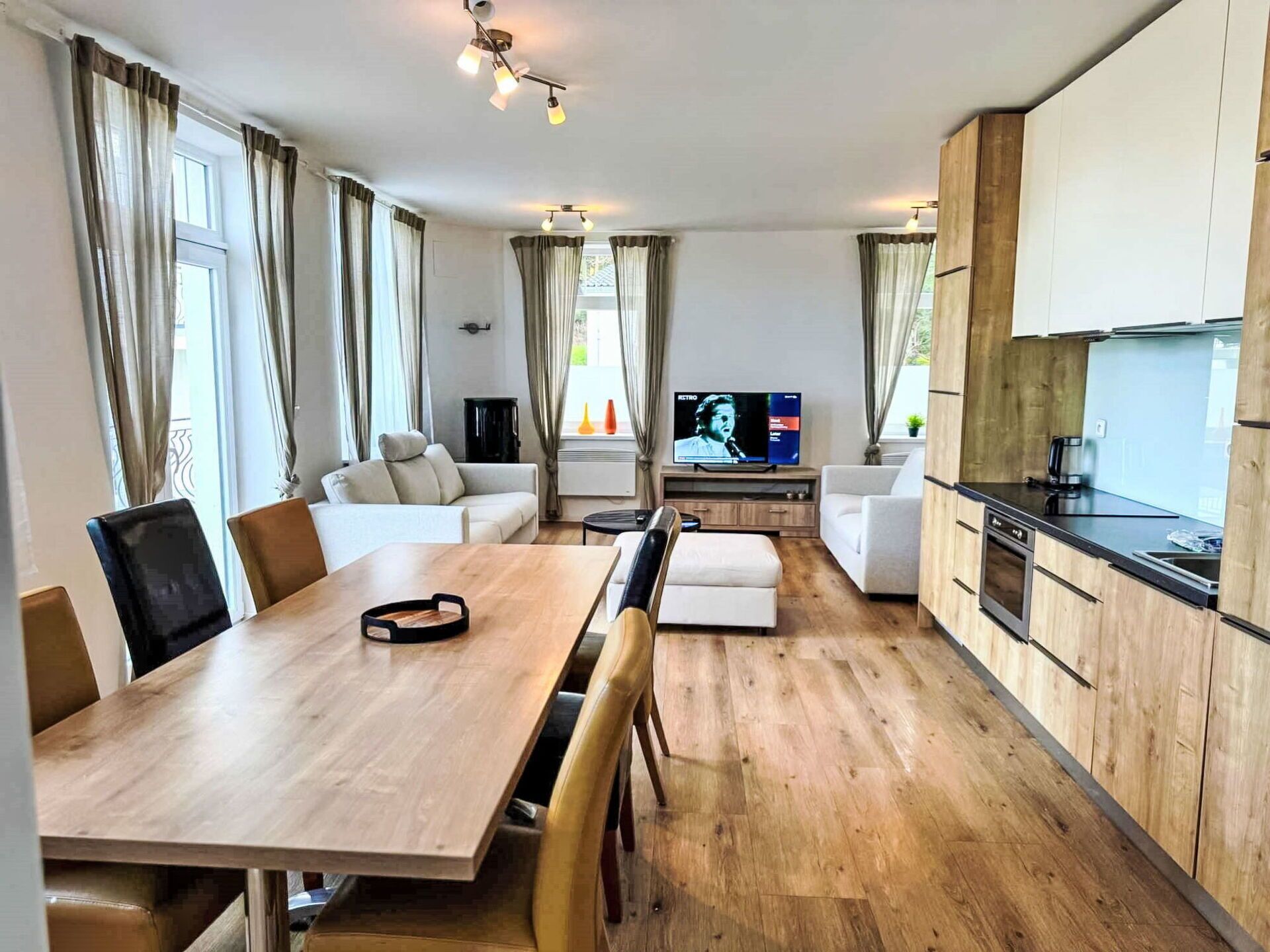 A modern living room with a wooden dining table, sofas, and a TV.