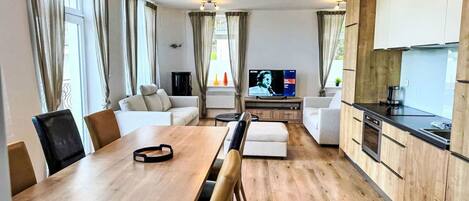 A modern living room with a wooden dining table, sofas, and a TV.