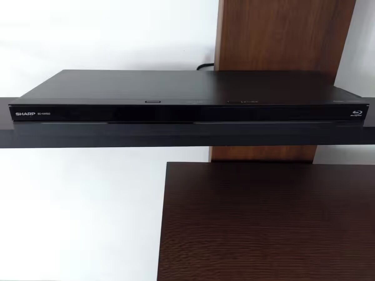 Een zwart elektronisch apparaat, mogelijk een dvd-speler, bevestigd aan een houten plank.