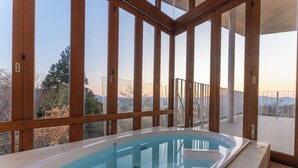 Ein moderner, überdachter Pool mit Holzrahmen und Glastüren, der einen Blick auf eine Berglandschaft bietet.