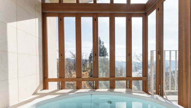 Ein Whirlpool mit Holzrahmen und Blick auf Berge durch große Fenster.