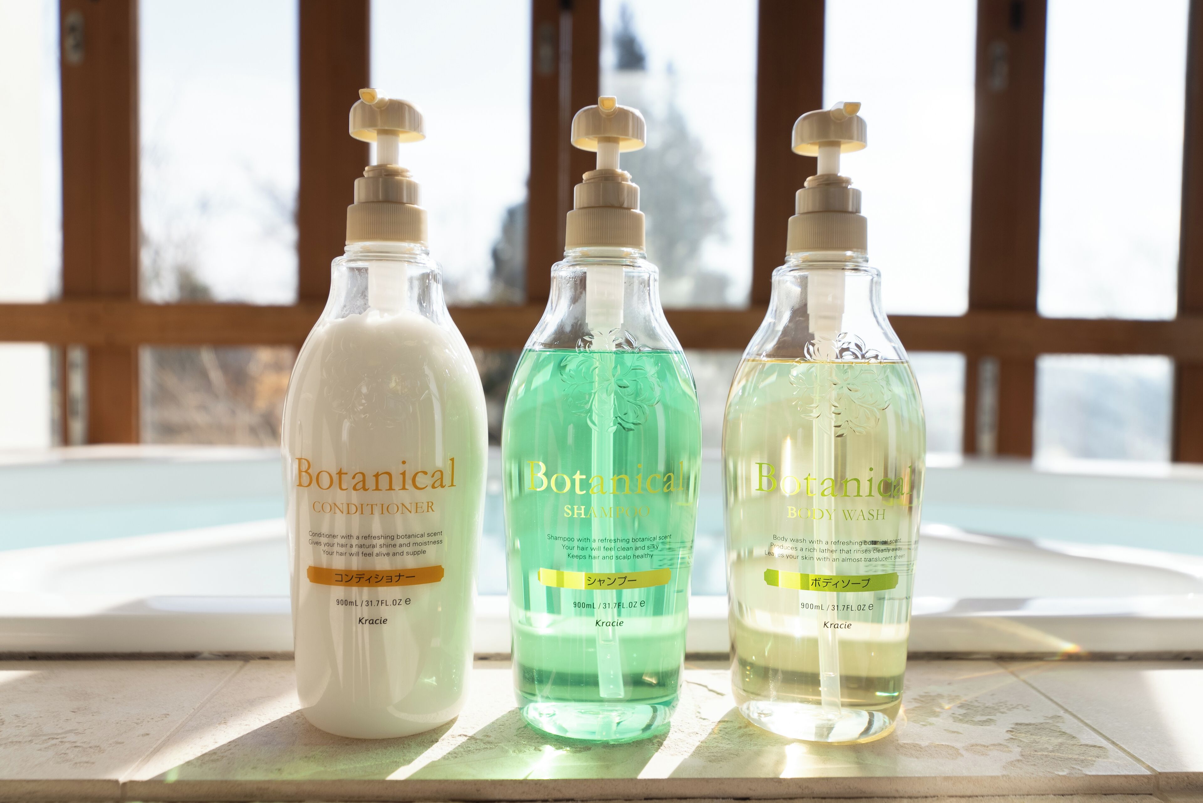 Trois bouteilles de produits de la gamme Botanical sont posées sur une surface carrelée, près d’une fenêtre donnant sur un bâtiment.