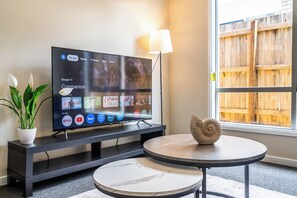 Televisor de pantalla plana sobre un suport, amb una selecció d'aplicacions de streaming, una planta en test i una closca decorativa sobre una taula rodona.