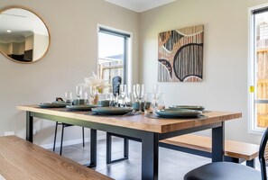A dining area with a wooden table set for four, a bench, and a modern abstract painting on the wall. - New 4-Bedroom Family Home with Carpark in Griffin (Griffin)