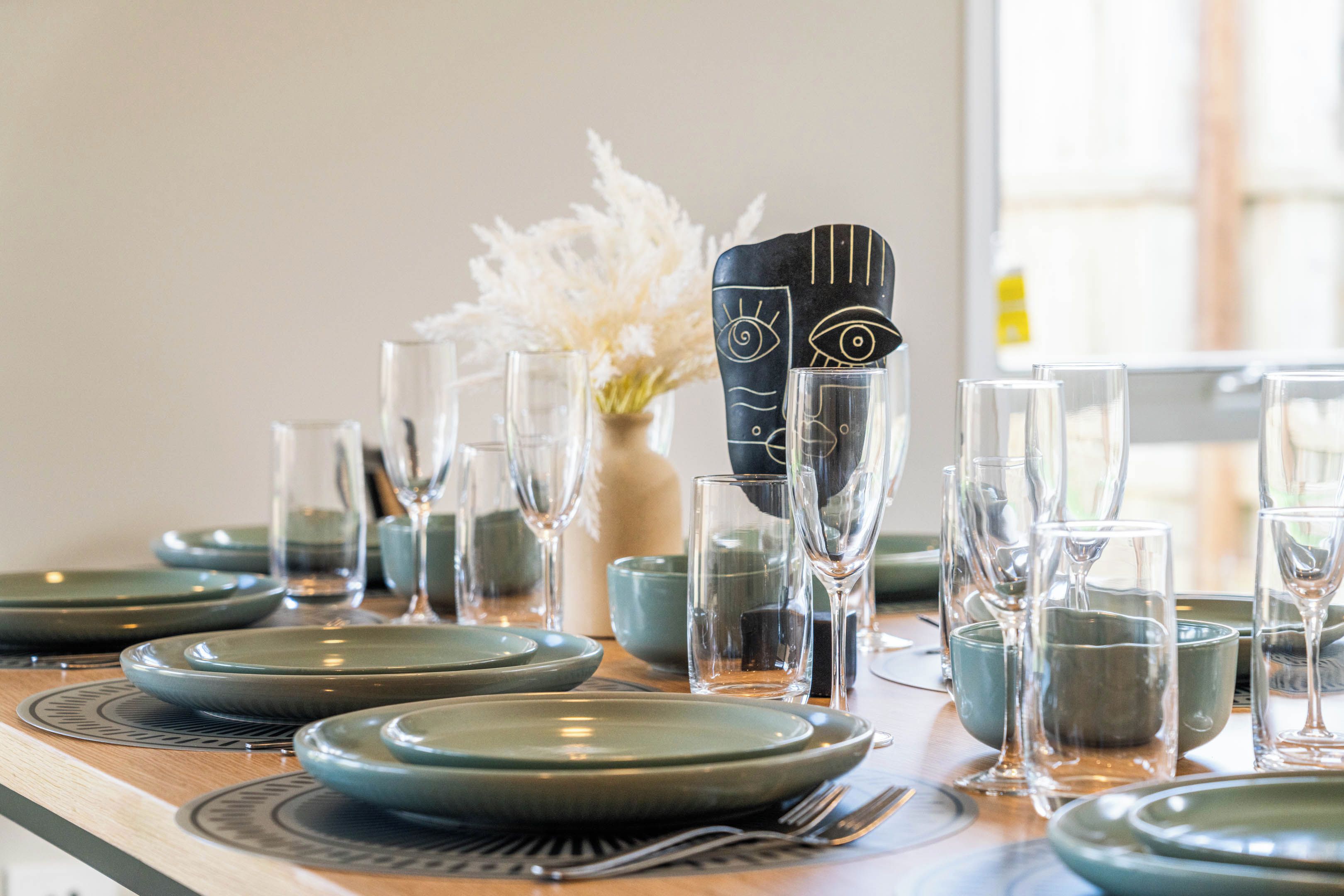 A table set with plates, glasses, and cutlery, with a decorative black vase and white flowers in the background.