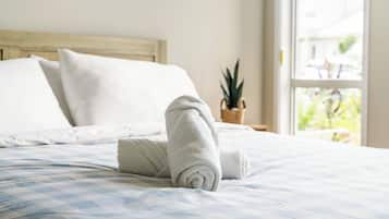 A neatly made bed with a rolled towel, a wooden headboard, and a window with a view of greenery.