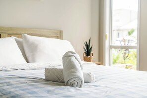 A neatly made bed with a rolled towel, a wooden headboard, and a window with a view of greenery. - New 4-Bedroom Family Home with Carpark in Griffin (Griffin)