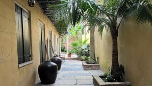A narrow alleyway with stone flooring, large vases, and potted plants. - Luxurious Rooftop French Quarter Penthouse (New Orleans)
