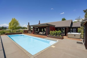 Une piscine avec un patio couvert, un jacuzzi et une cheminée en pierre.