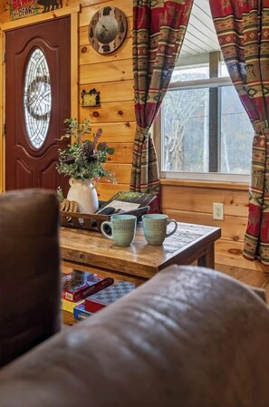 Ein gemütliches Blockhaus-Interieur mit einer Holztür, einem Fenster mit Vorhängen, einem Tisch mit Krug, Tasse und Büchern.