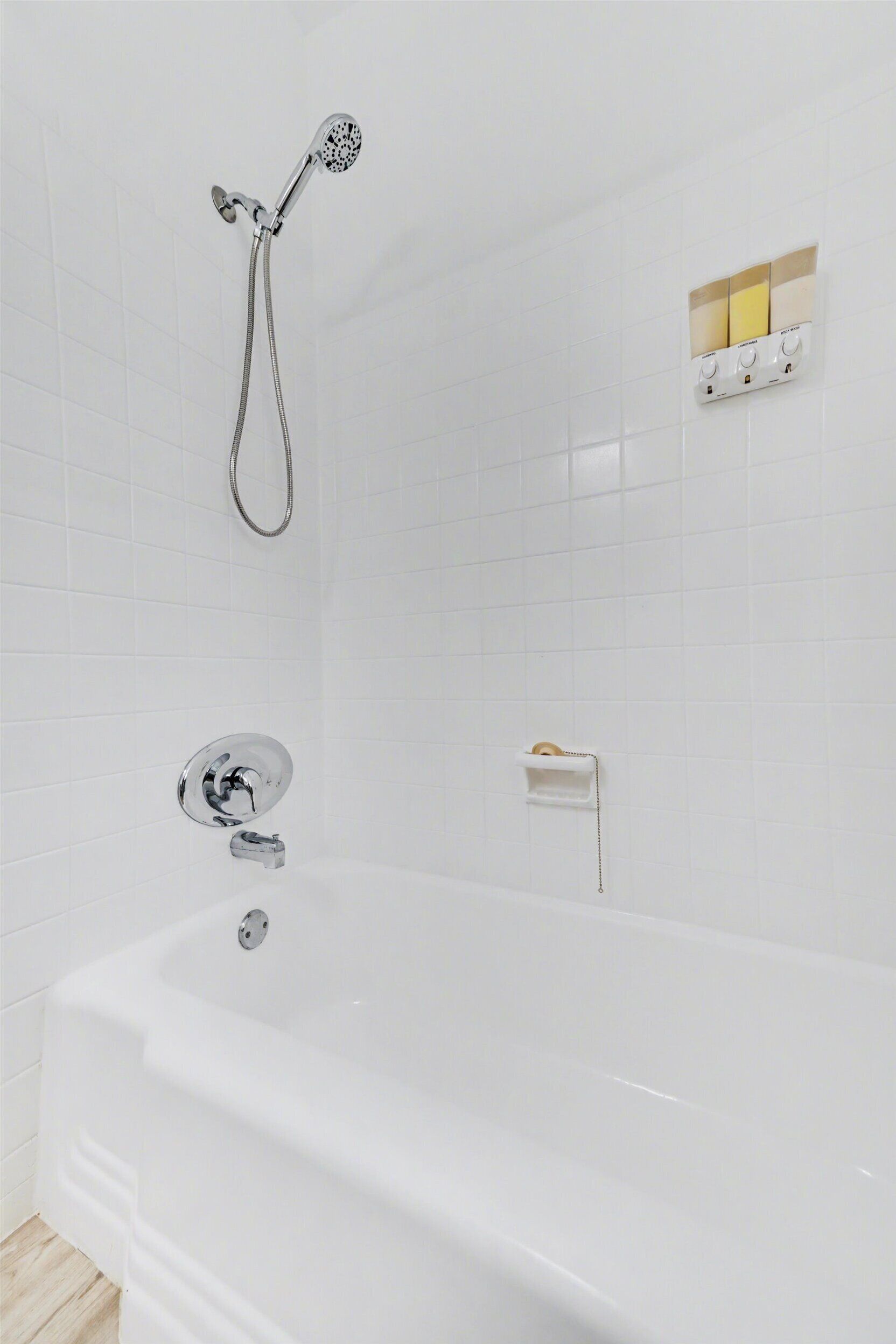 Un baño moderno con una bañera blanca, un cabezal de ducha de mano y un panel de control en la pared.
