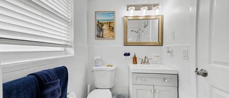 A bathroom with a toilet, sink, and mirror. There is a towel hanging on the wall and a picture frame above the mirror.