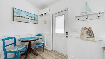 A dining area with a wooden table and two blue chairs, a white door, and a wall-mounted shelf with a sailboat decoration.