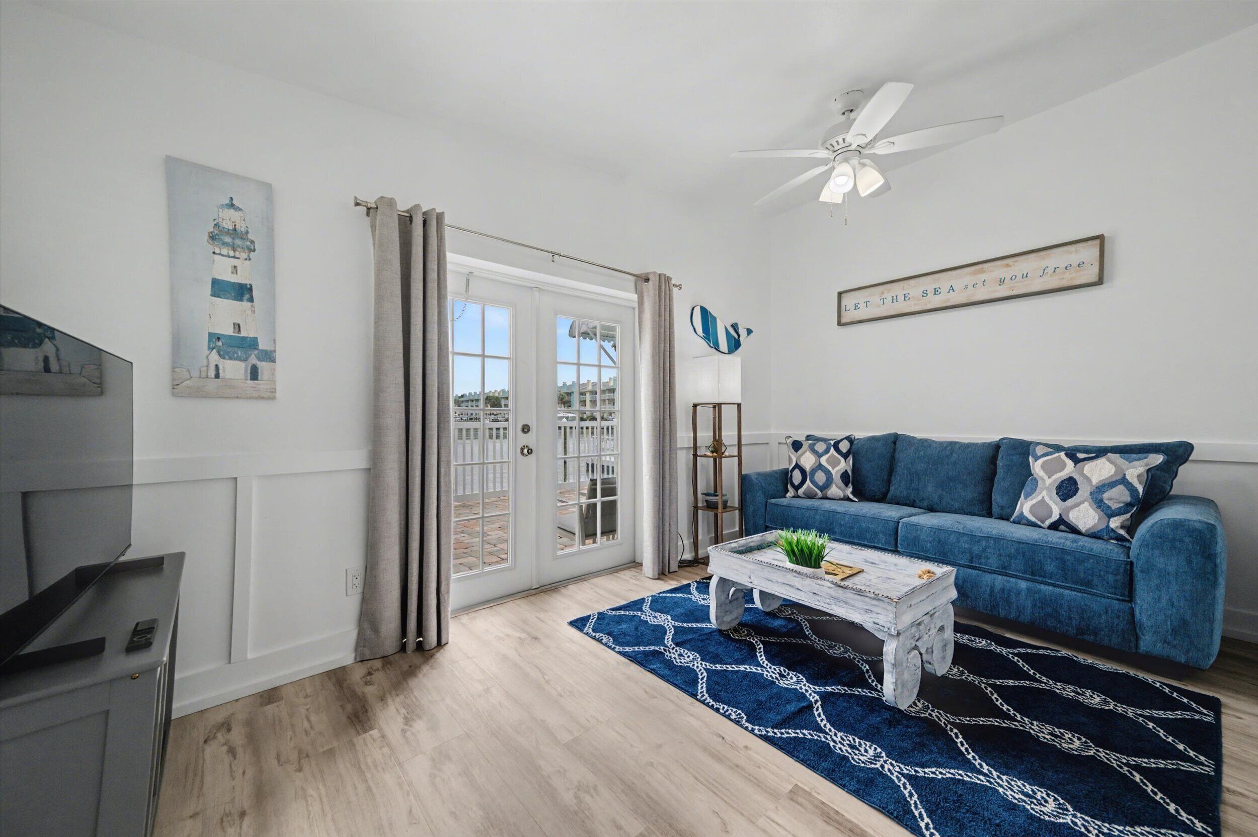 A living room with a blue sofa, a coffee table, a ceiling fan, and a door leading to a balcony.