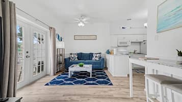 A modern living room with a blue sofa, a white coffee table, and a kitchen area with white cabinets and a microwave.
