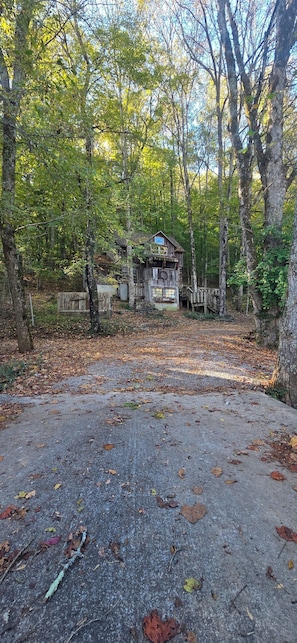A rustic cabin with a wooden deck, surrounded by a forest.