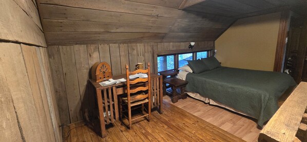 Un dormitorio de cabaña de madera con cama, escritorio, silla y ventanas.