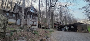 A rustic wooden cabin with a large wheelhouse, a covered carport, and a gravel driveway.