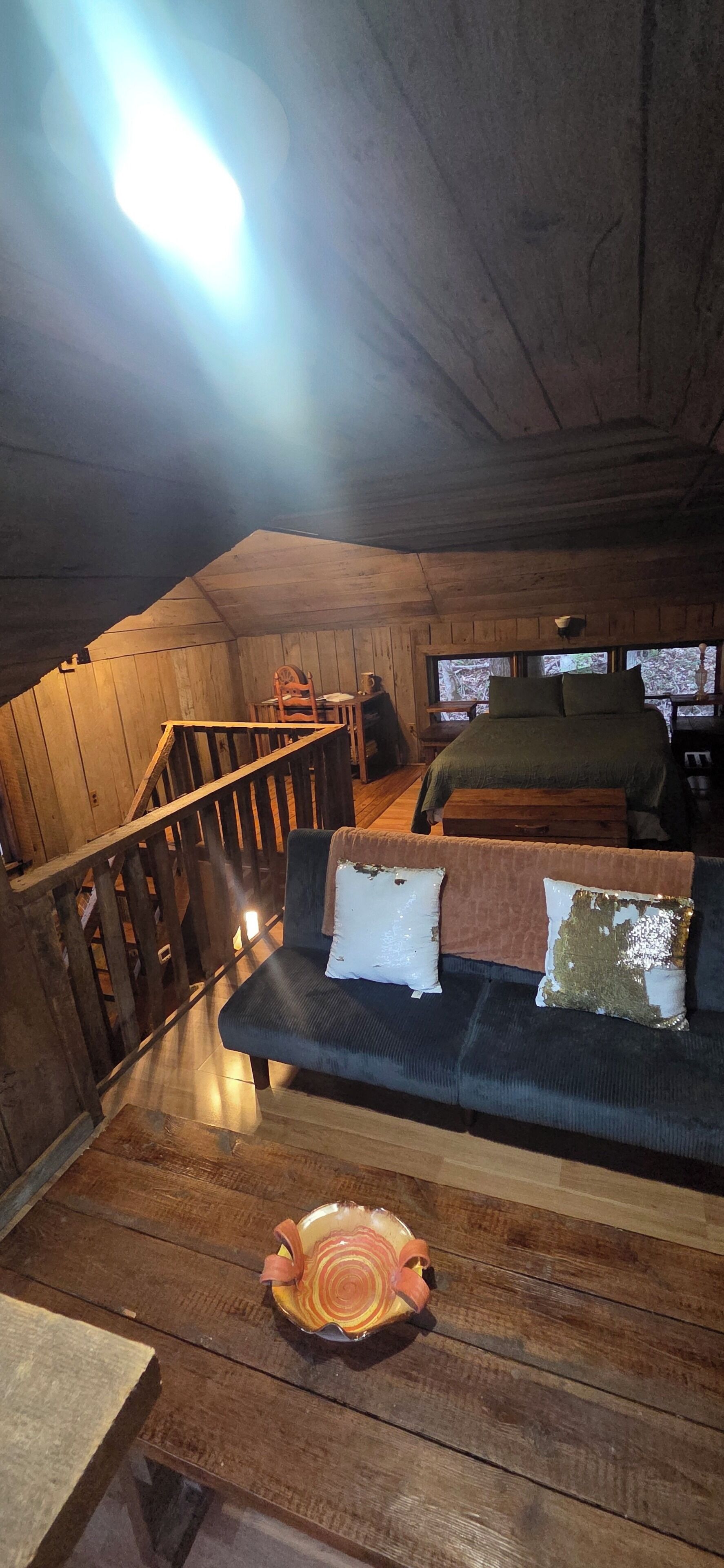 Ein gemütliches Schlafzimmer unter dem Dach mit einer Holztreppe, einem Bett, einer Couch und einem Esstisch.