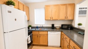 A compact kitchen with wooden cabinets, a white refrigerator, a microwave, and a dishwasher. - The Arbor's Haven - Cozy, Stylish Retreat Steps from Downtown Ann Arbor (Ann Arbor)