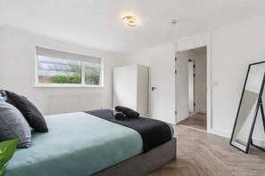 A bedroom with a bed, a window, a radiator, a wardrobe, and a mirror. - Modern 3 bed house in Edmonton with driveway parking (London)