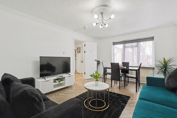 A living room with a TV, sofa, dining table, chairs, and a plant. - Modern 3 bed house in Edmonton with driveway parking (London)