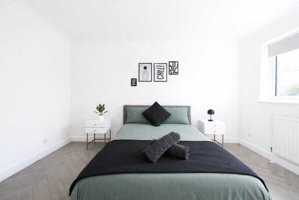 A bedroom with a bed, two bedside tables, a window, and wall art. - Modern 3 bed house in Edmonton with driveway parking (London)