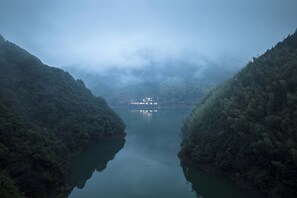 A river flanked by dense forest, with a boat docked on the riverbank. - LOST LODGE Shendu Wubei Lin'an (Hangzhou)