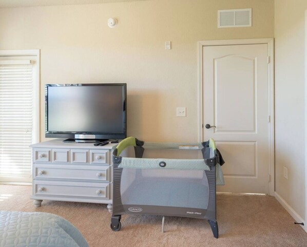 A room with a television on a dresser, a crib with a playpen, and a door. - Bright 3BR Resort Condo Near Disney + Pools (Davenport)