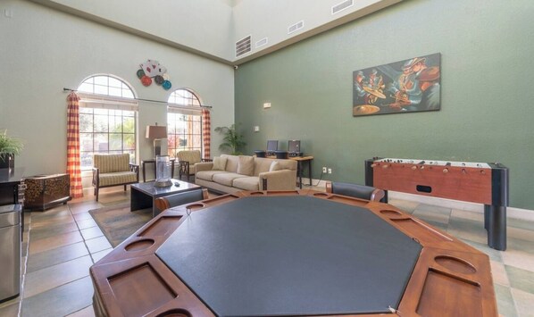 A spacious room with a foosball table, comfortable seating, and a large window with curtains. - Bright 3BR Resort Condo Near Disney + Pools (Davenport)