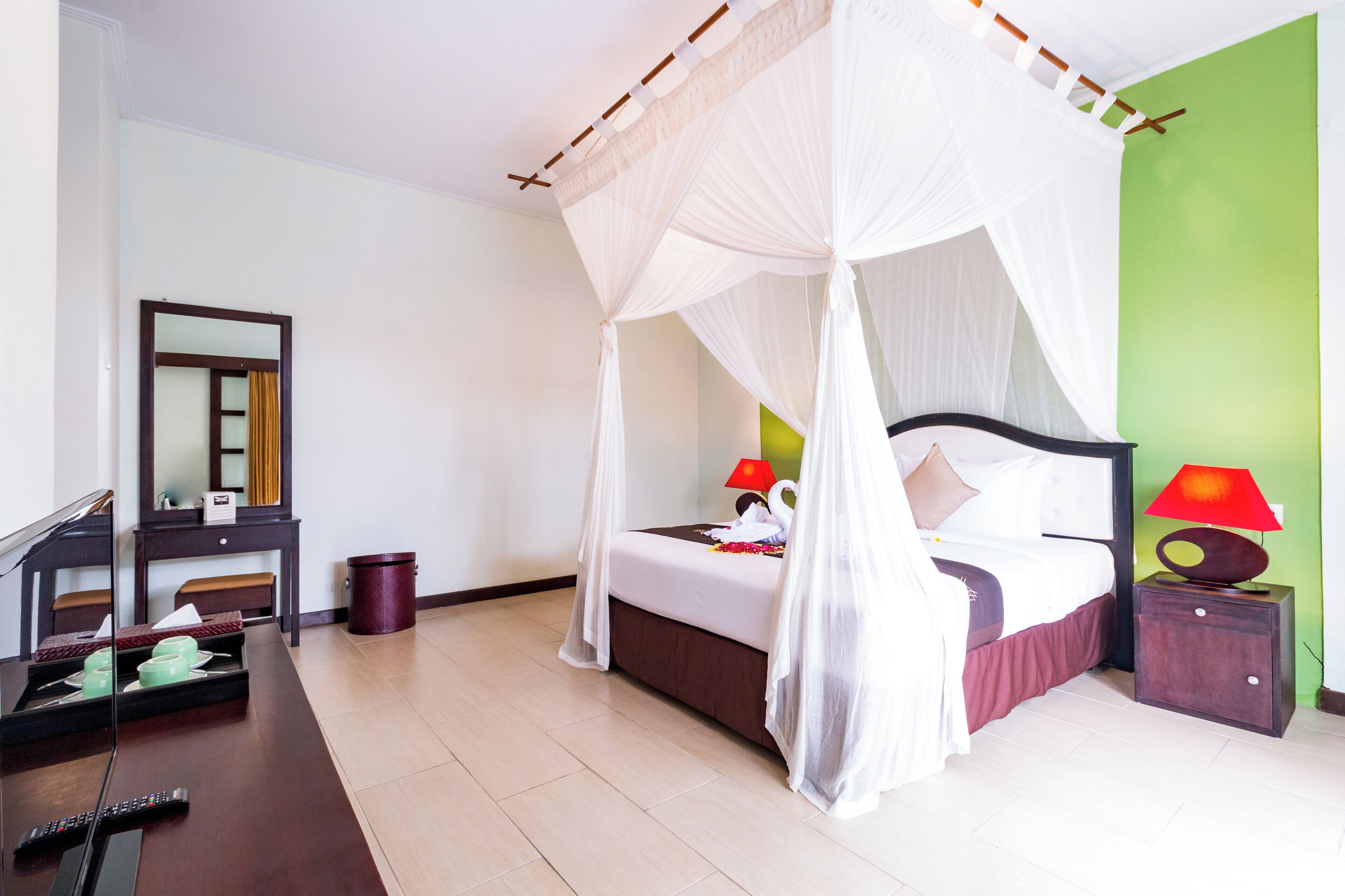 Habitación de hotel con cama, lámparas de noche, mesita de noche, espejo, cómoda y basurero.