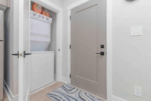 Un pasillo con una puerta, un armario blanco con estufa y un tapete estampado.