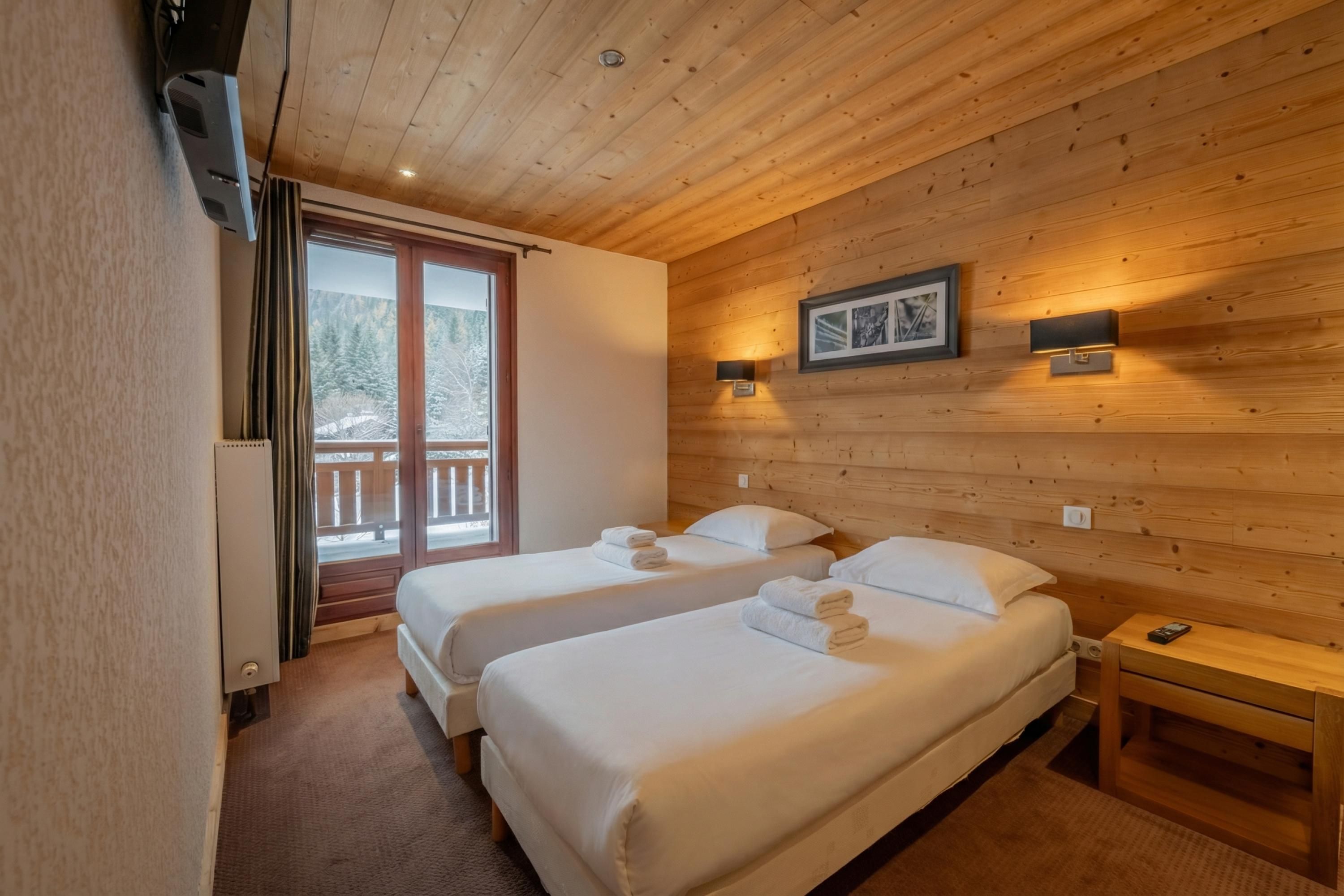 Een kamer met twee bedden, een houten plafond, een raam met uitzicht op bomen en een aan de muur hangend schilderij.