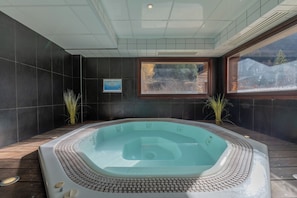 Ein Whirlpool mit Fliesenverkleidung, einer Holzdar Terrasse und Blick auf eine verschneite Landschaft durch ein Fenster.