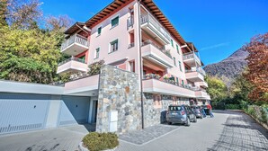 A multi-story hotel with balconies, a stone facade, and a parking area. - Appartamento Residenza Chiara: Sunny Balcony and Mountain View, Laveno Mombello, Italy (Laveno Mombello)