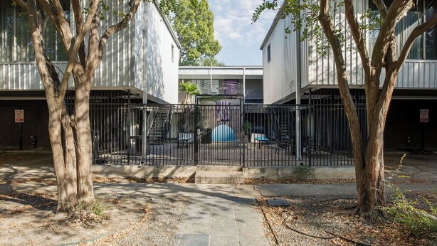 Un cortile recintato con alberi, un vialetto e un edificio con un balcone.