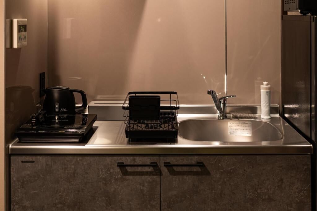 A kitchen with a coffee maker, a dish rack, a sink, and a refrigerator.