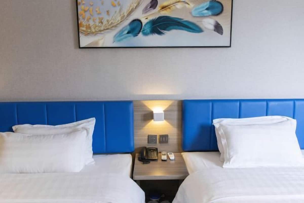 A hotel room with two beds, a blue headboard, a bedside table with a phone, and a wall-mounted light.