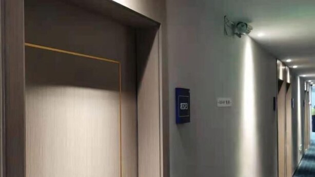 A hotel corridor with a blue carpet, a door on the left, and a sign on the wall. - 7 Days Premium Hotel (Beijing Qinghe Yongtaizhuang Metro Station) (Beijing)
