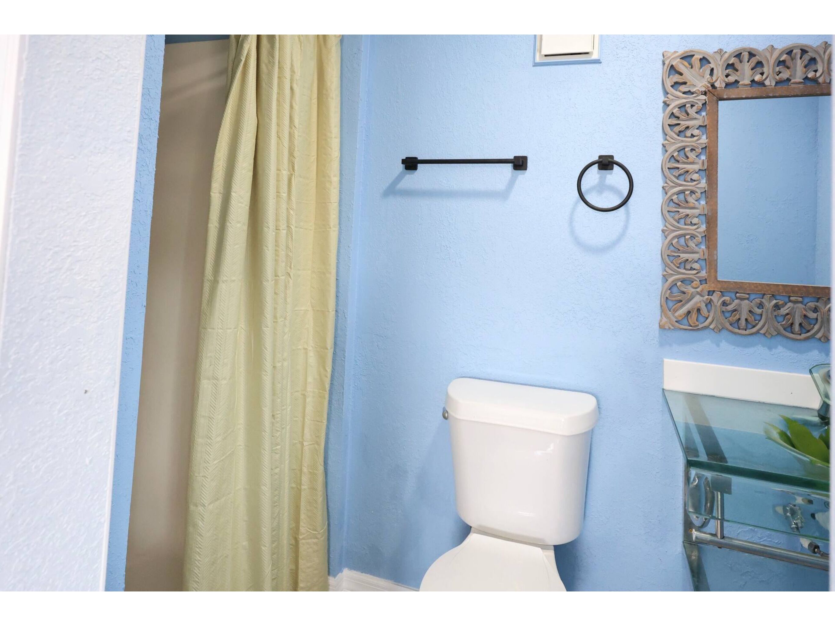 A bathroom with a toilet, a towel rack, a glass shower enclosure, and a decorative mirror.