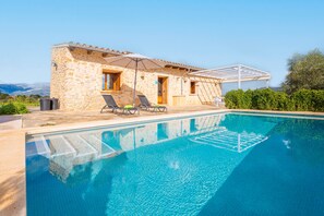 A stone villa with a swimming pool, outdoor seating, and a view of the mountains.