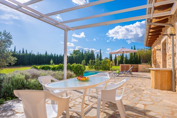 An outdoor patio with a table and chairs, a pool, and a stone floor.
