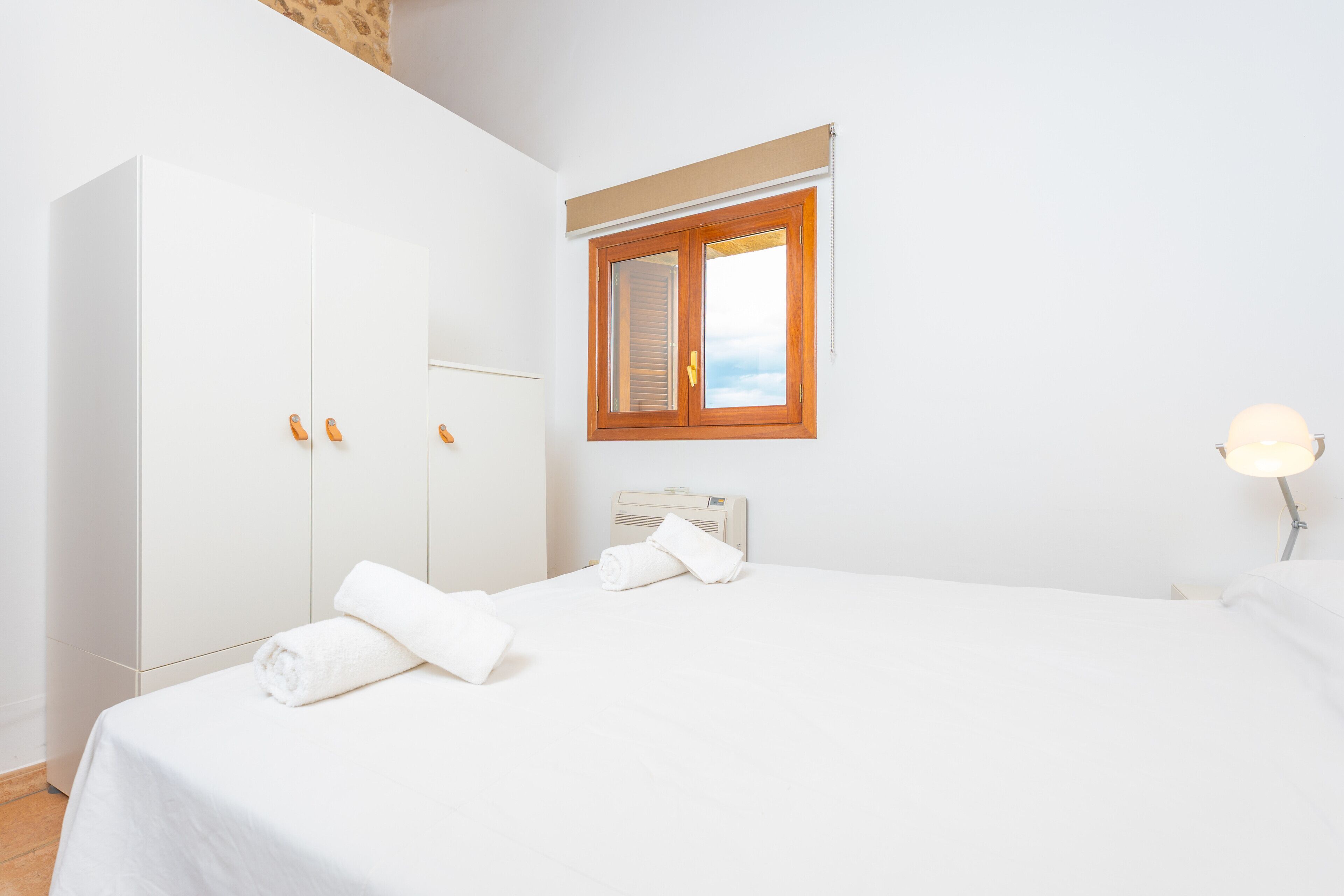 Habitación de hotel con una cama grande, un armario, una mesita de noche, una lámpara y una ventana con contraventanas.
