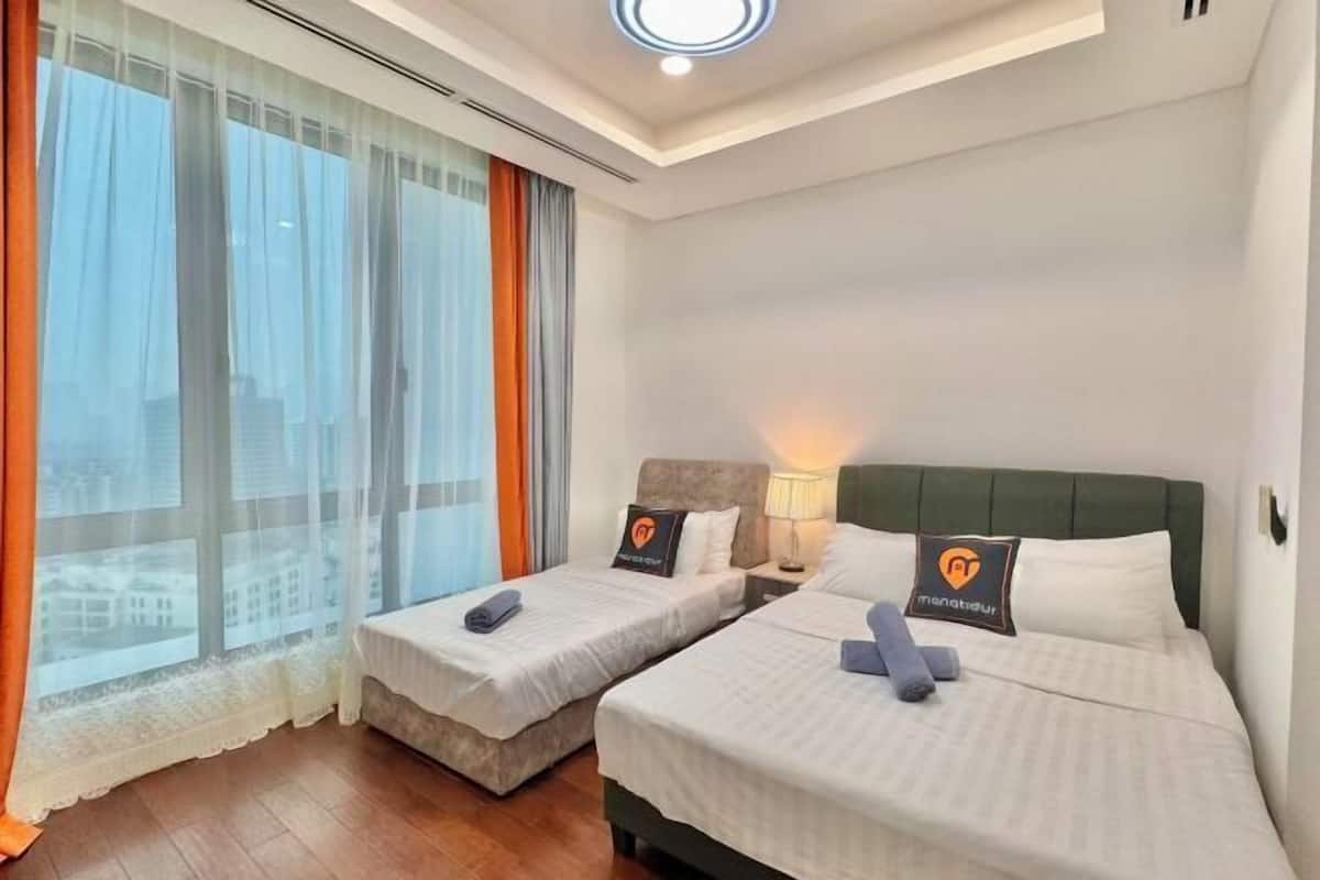 Habitación de hotel con dos camas, un ventanal con cortinas translúcidas y vistas a la ciudad.