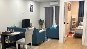 A modern living room with a sofa, a dining table, and a TV. - The Cozy Haven (Halifax)