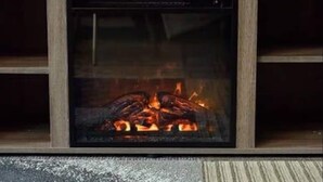 A fireplace with a glass front, wooden frame, and visible burning logs. - Blue&Gold Art Deco 2BR1BA Loft close to Genentech (South San Francisco)